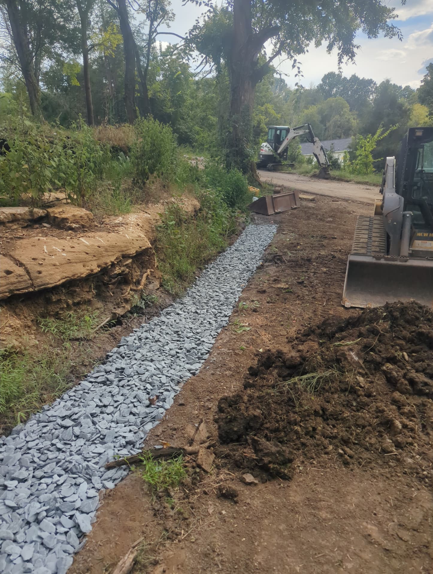 French drain construction with drainage stone along a wooded hillside