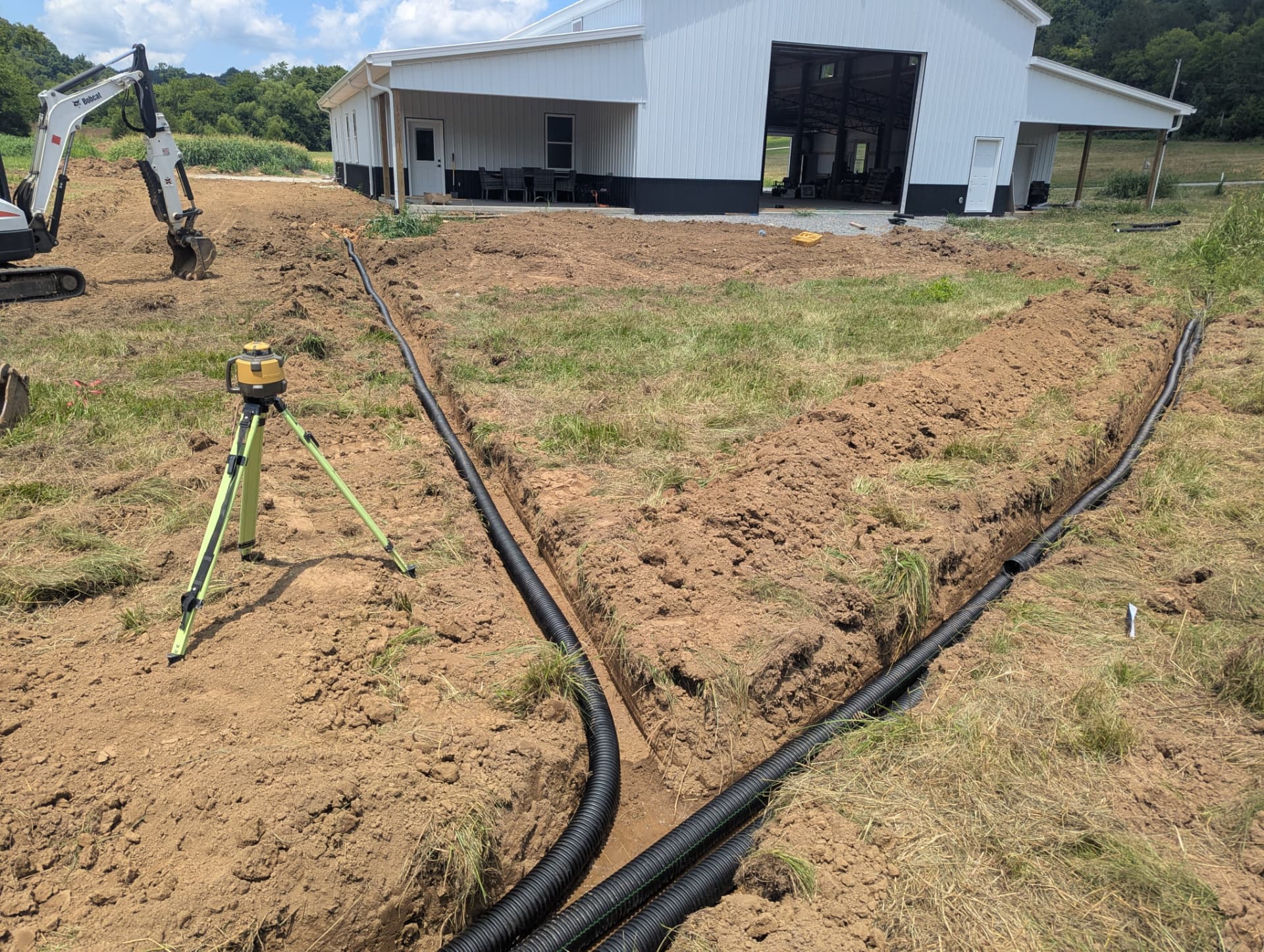 Multiple corrugated drainage lines laid out in open trenches beside a residential building