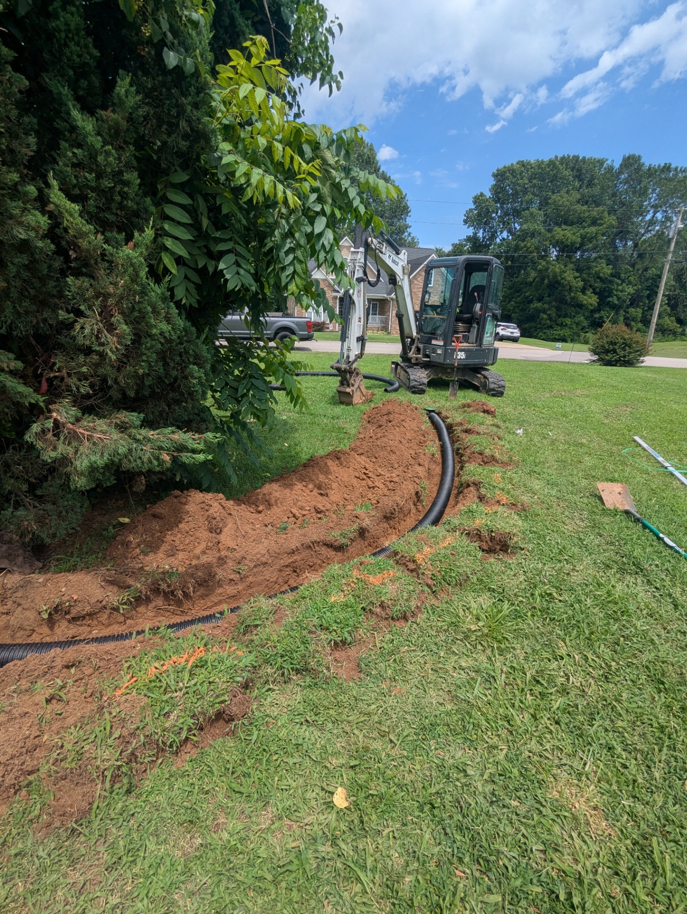 Bobcat mini-excavator installing a buried downspout extension pipe in a residential Middle Tennessee yard