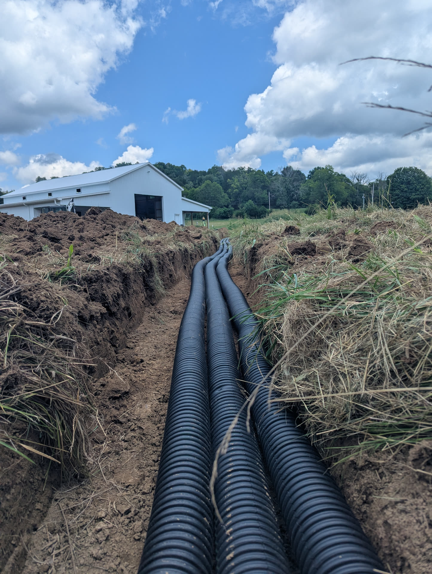 Multiple black corrugated drainage pipes running along the bottom of a freshly excavated trench toward a residential building in Middle Tennessee