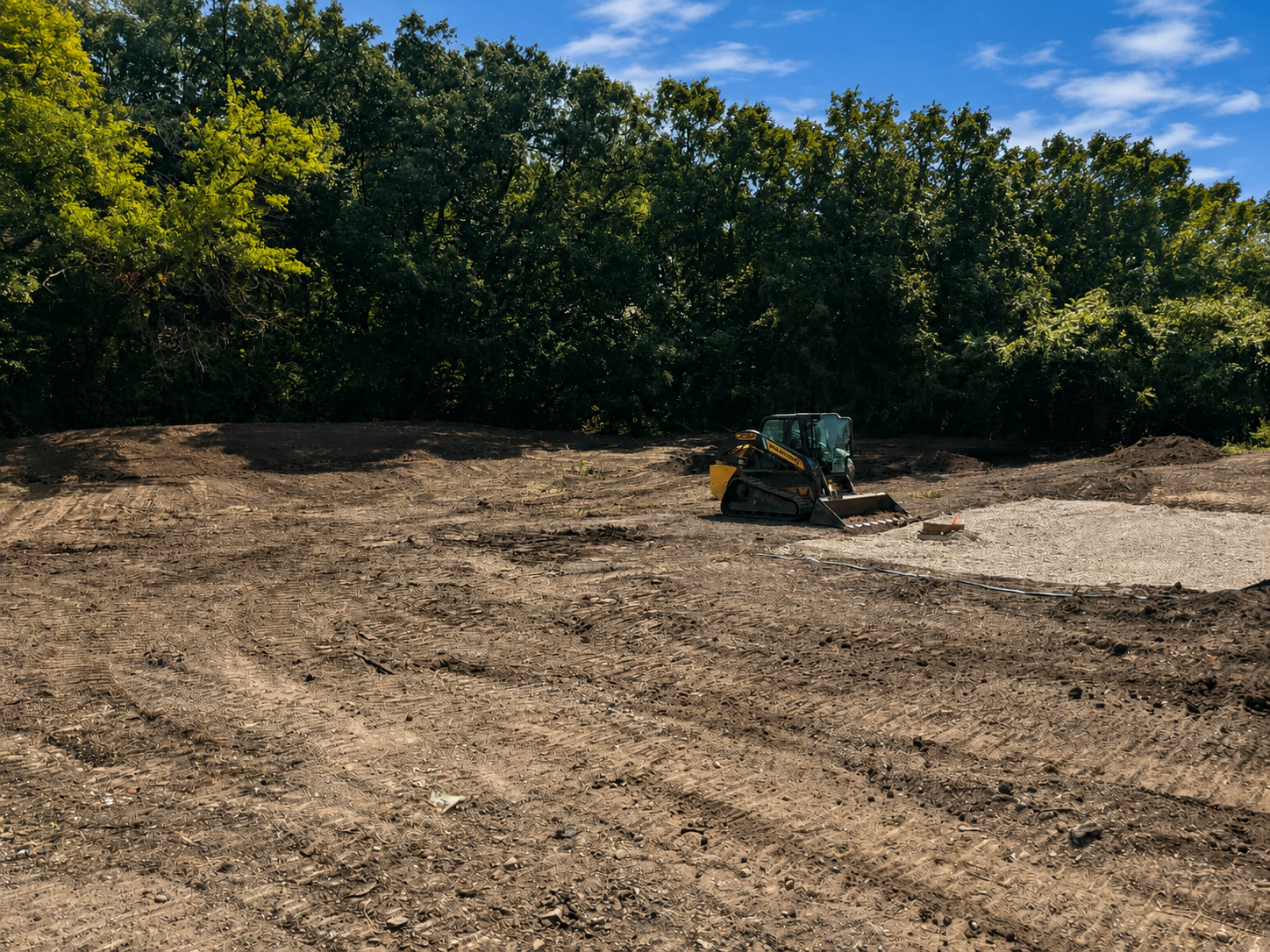 Wide cleared grading site with a track loader shaping the ground beside a wooded tree line in Middle Tennessee