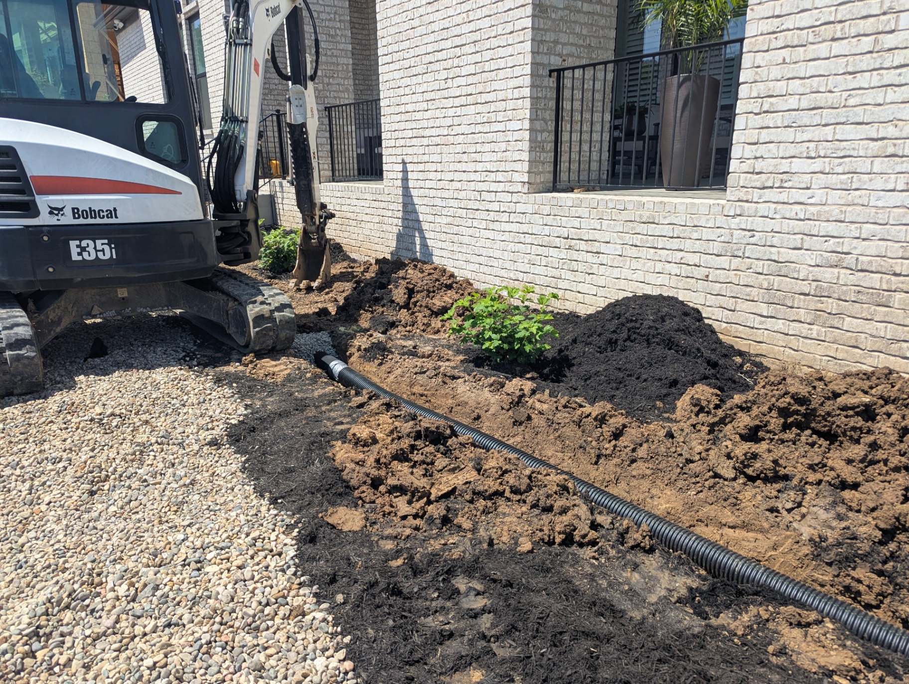 Bobcat E35i mini excavator installing a buried downspout extension drain line along a Franklin TN home foundation