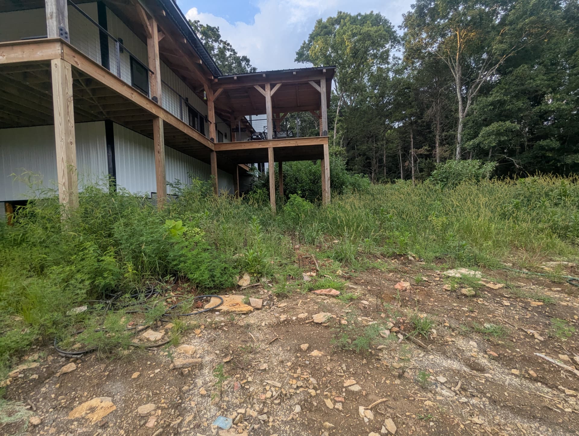 Overgrown future greenhouse area and natural drainage path beside new home before grading